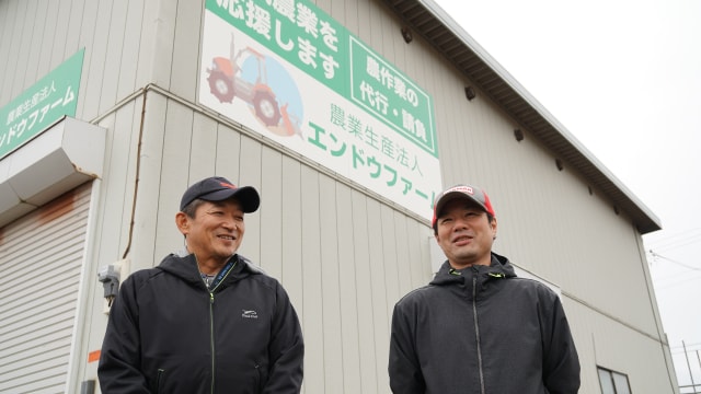 「地域農業を応援します」と格納庫の看板にも大きくアピール。目指す農業の夢を語り合う遠藤直道さん(左)と遠藤誠さん(右)